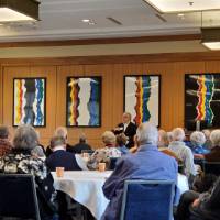 A man speaks to people seated at round tables